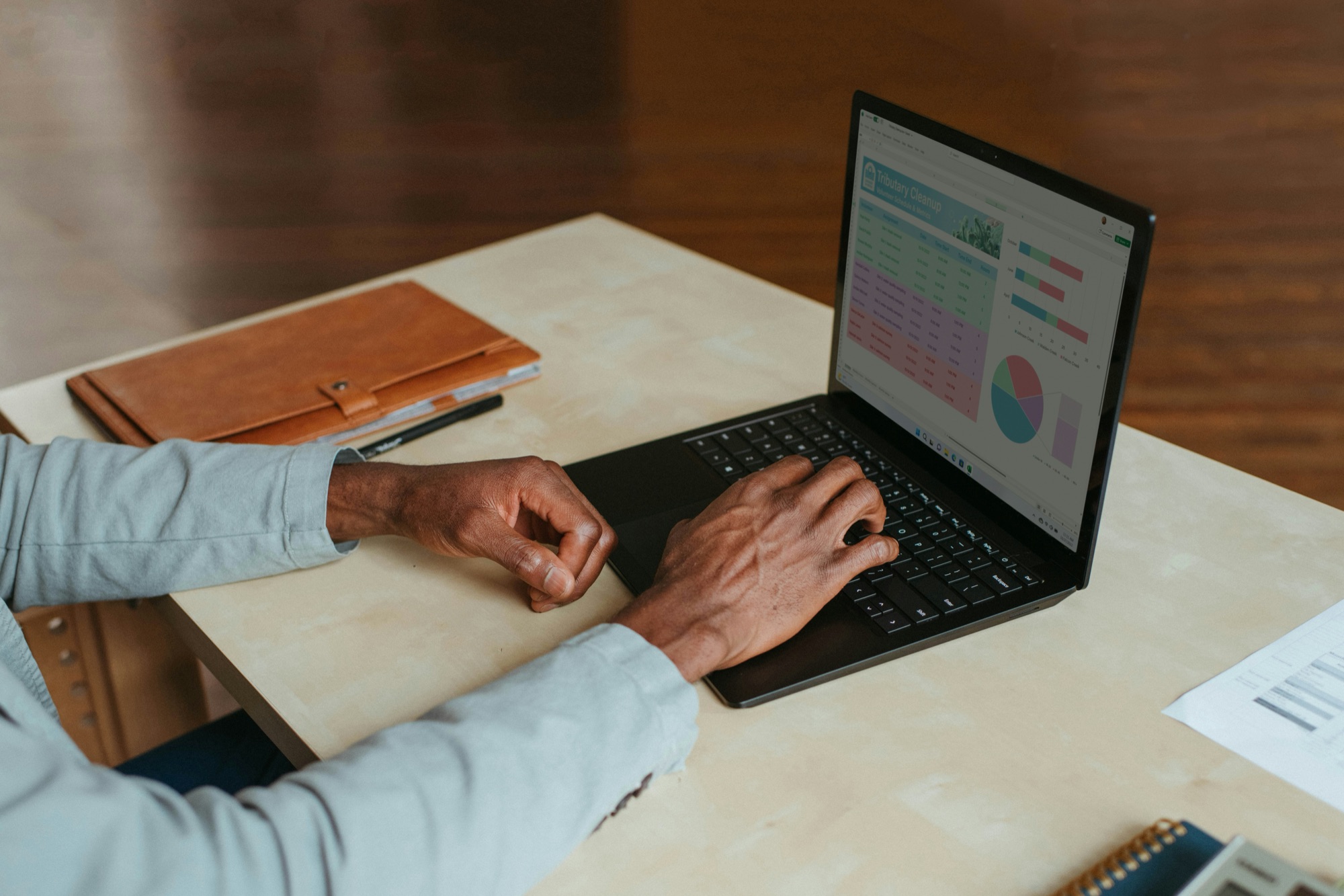Hands typing on a laptop showing charts, on a wooden desk