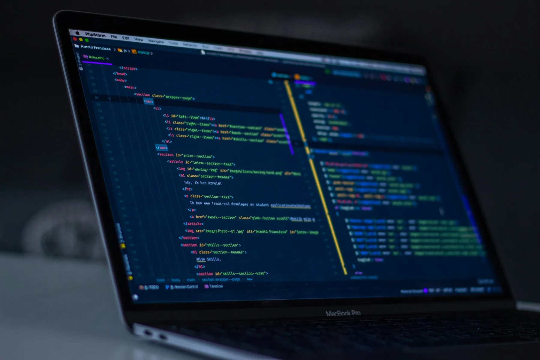 A laptop on a dark desk with code in an editor on the screen.
