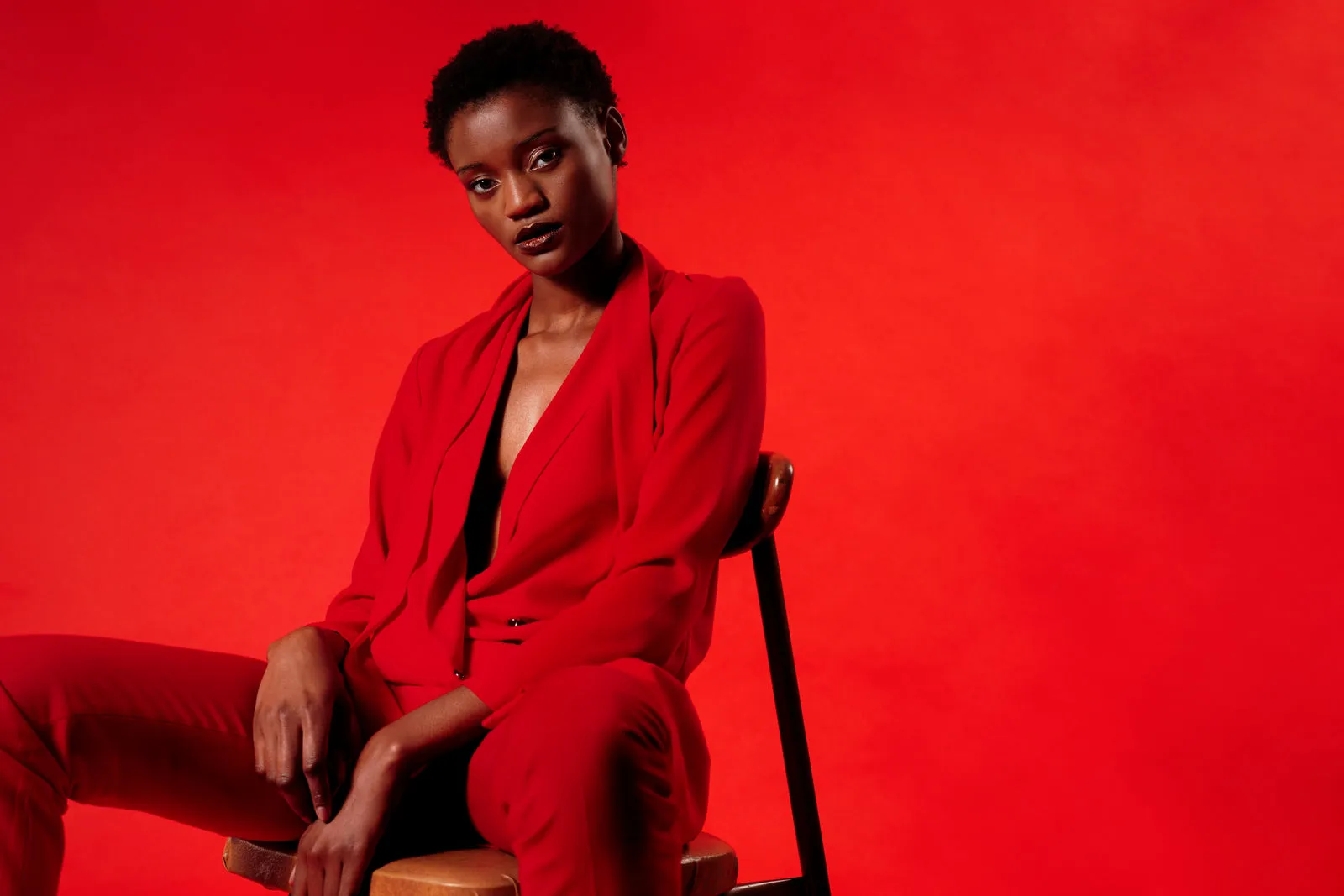 A model in a red trouser suit sitting against a red wall.