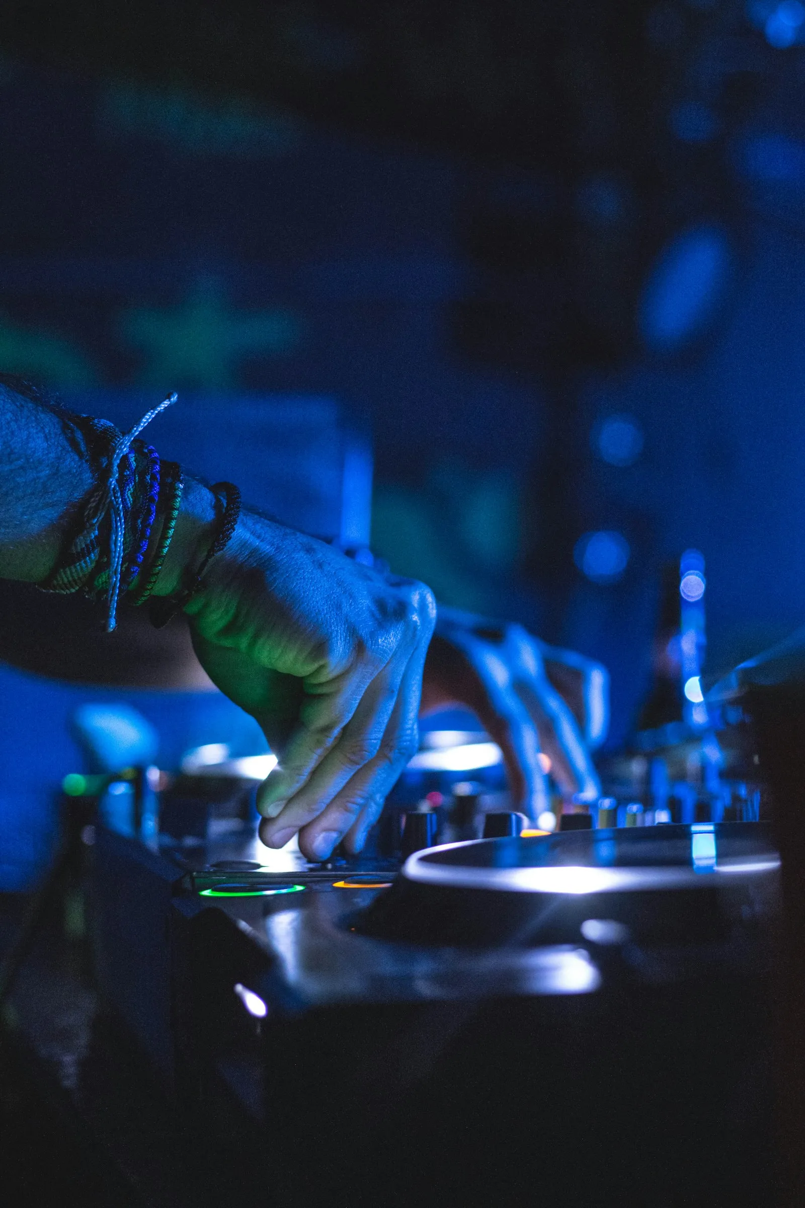 A DJ's hands on a controller under blue club lights.