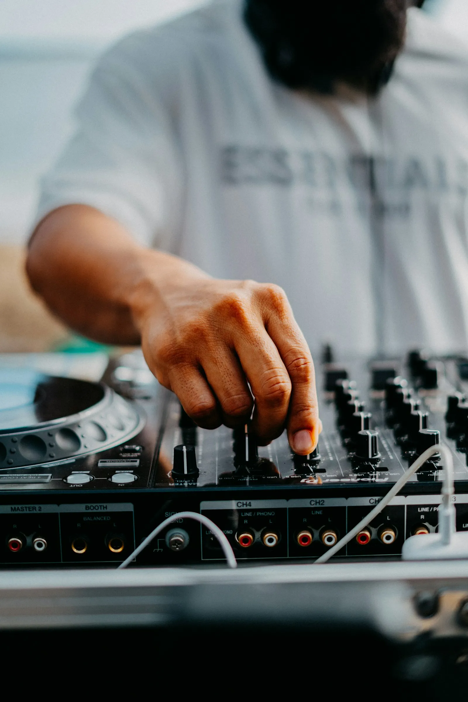 A DJ in a white T-shirt adjusting a mixer next to a turntable.