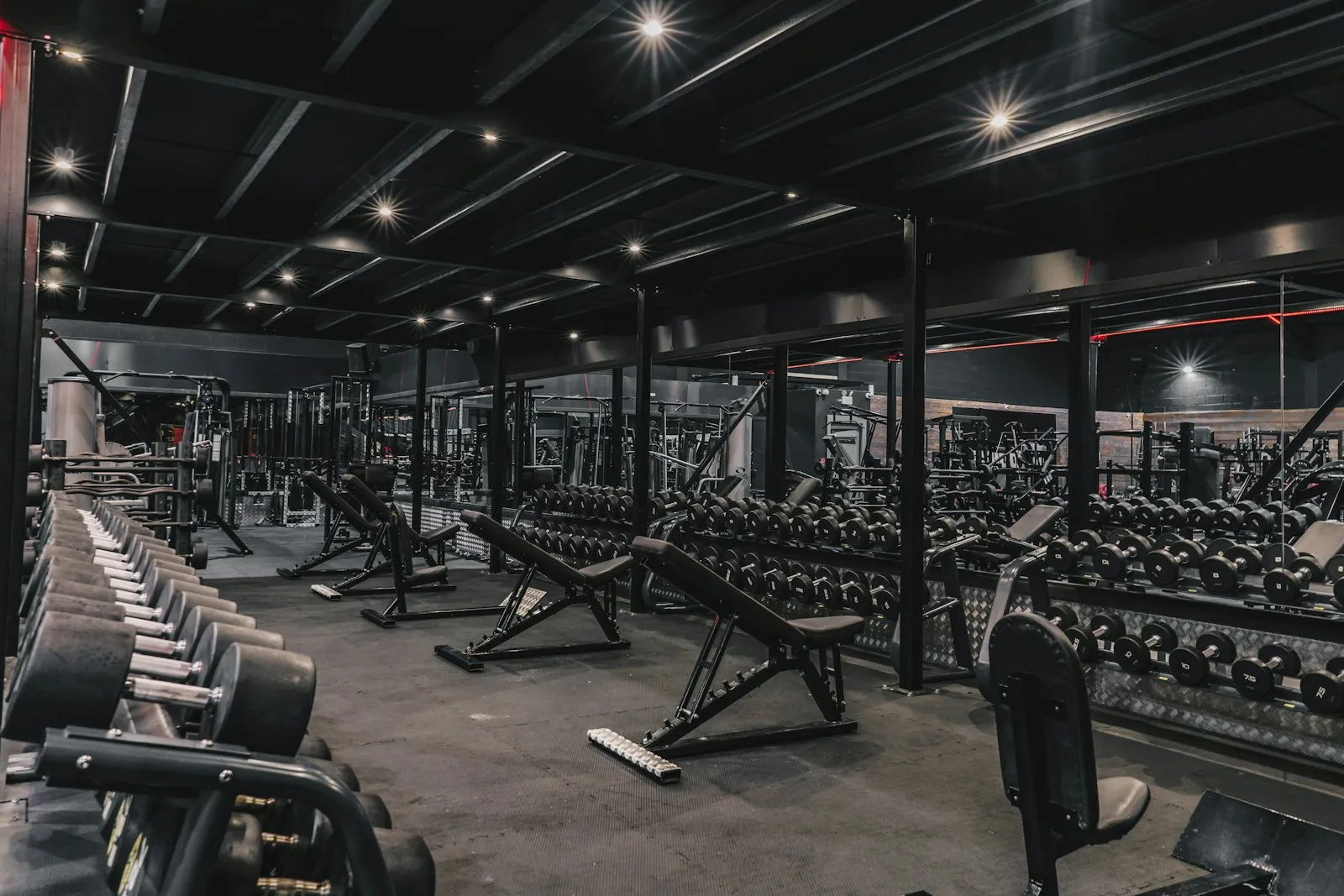 A dark gym with rows of racks, benches and dumbbells.
