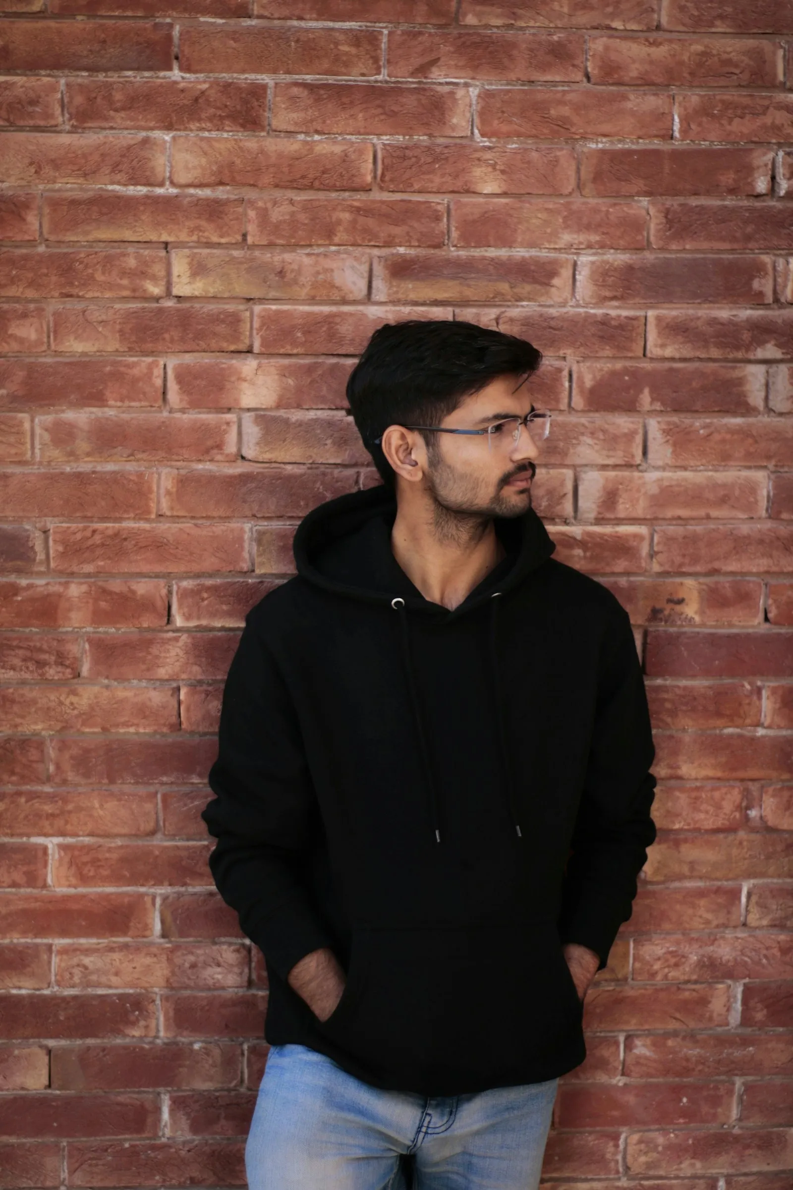 A man in a black hoodie leaning against a brick wall.