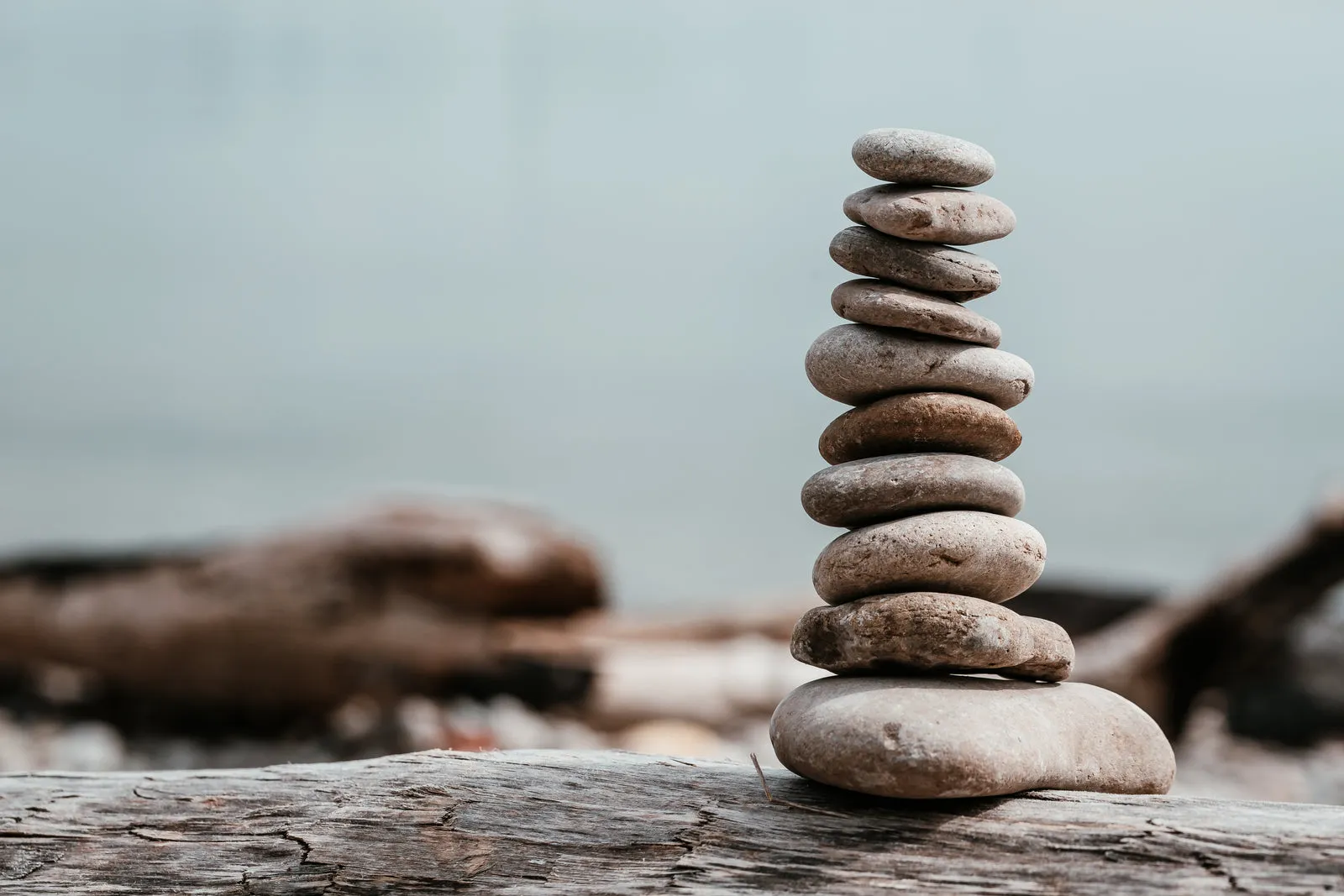 A stack of smooth grey stones balanced on driftwood by the water.