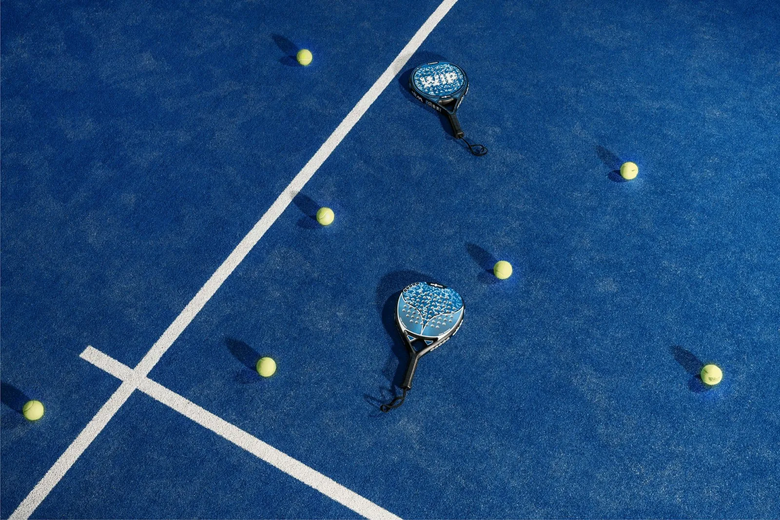 Padel rackets and balls on a blue court, seen from above.